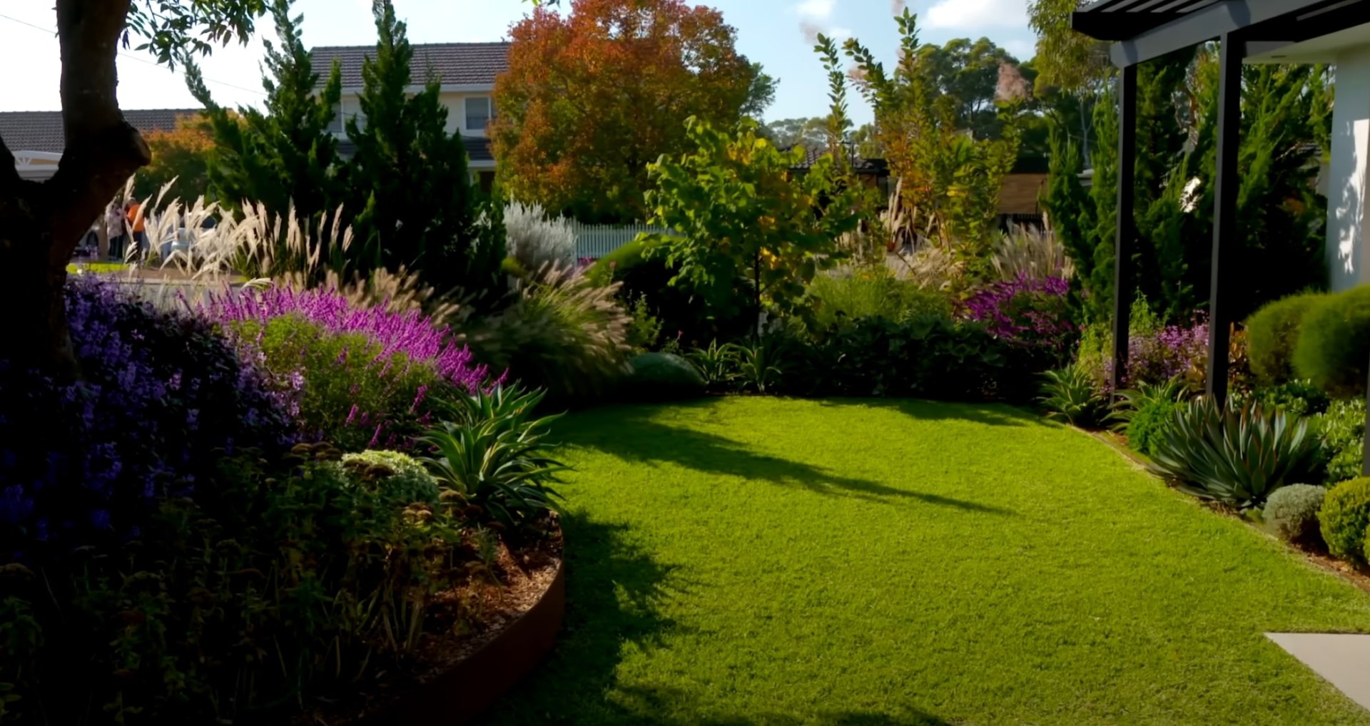Professional landscape design featuring diverse plantings and pristine lawn maintenance Colorful perennial garden with purple and white flowers, ornamental grasses, and perfect lawn